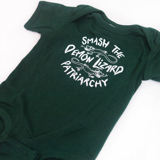 close up angled image of an emerald green tri blend baby onesie on a white background. onesie has center chest print in white that says smash the demon lizard patriarchy with two lizards