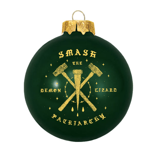 Double-sided dark green Christmas ornament by Devan Power featuring a gold graphic of two crossed hammers and a nail with the text Smash the Demon Lizard Patriarchy.