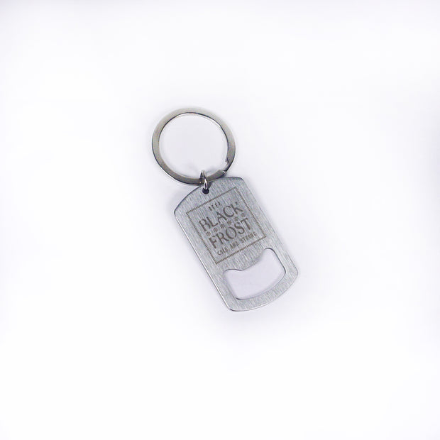 A silver metal keychain with a rectangular bottle opener engraved "BLACK FROST LOW CALORIE PREMIUM" is shown on a white background. The product is from Buffering the Vampire Slayer.