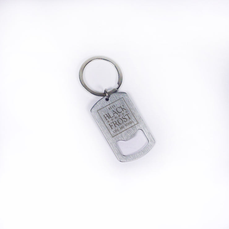 A silver metal keychain with a rectangular bottle opener engraved "BLACK FROST LOW CALORIE PREMIUM" is shown on a white background. The product is from Buffering the Vampire Slayer.