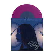 image of a signed side a of a purple seven inch vinyl record on a white background. side a's cover is on the bottom and has a womans face in front of clocks. 