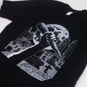 angled image of a black tee shirt on a white background. tee has a white print on the center chest of a hand holding a stake in a cemetary over a full moon. bottom left says buffering the vampire slayer