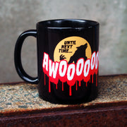 image of a black coffee mug. mug has full print in white and red that says AWOOOOOO! Above is an orange moon with a black Silhouette of a warewolf and the words until next time.