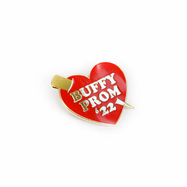 A limited edition red heart enamel pin from Buffering the Vampire Slayer, featuring a gold stake and white "BUFFY PROM 22" text.