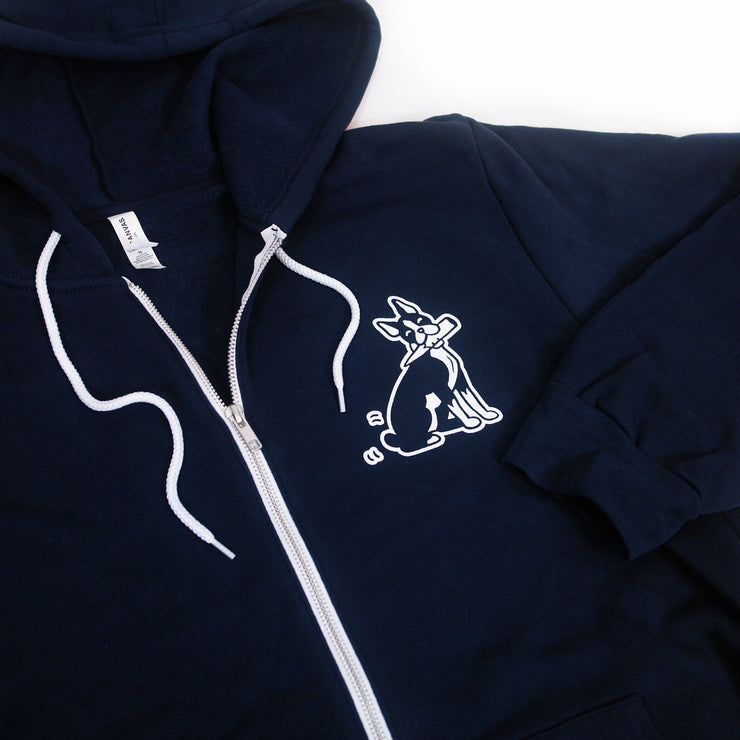 close up, angled image of the front of a navy zip up hoodie on a white background. front of the hoodie has a small chest print on the right of a dog with a wooden stake in its mouth.