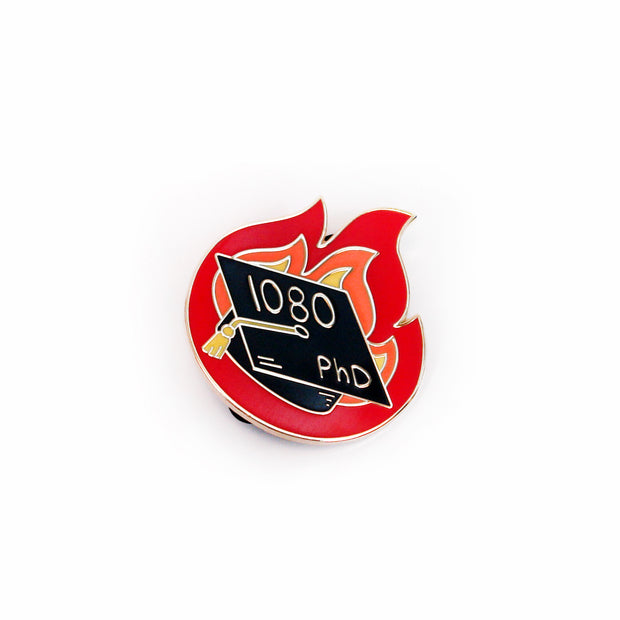 image of a enamel pin on a white background. pin is in the shape of fire and has a graduation cap that says 1080 PhD