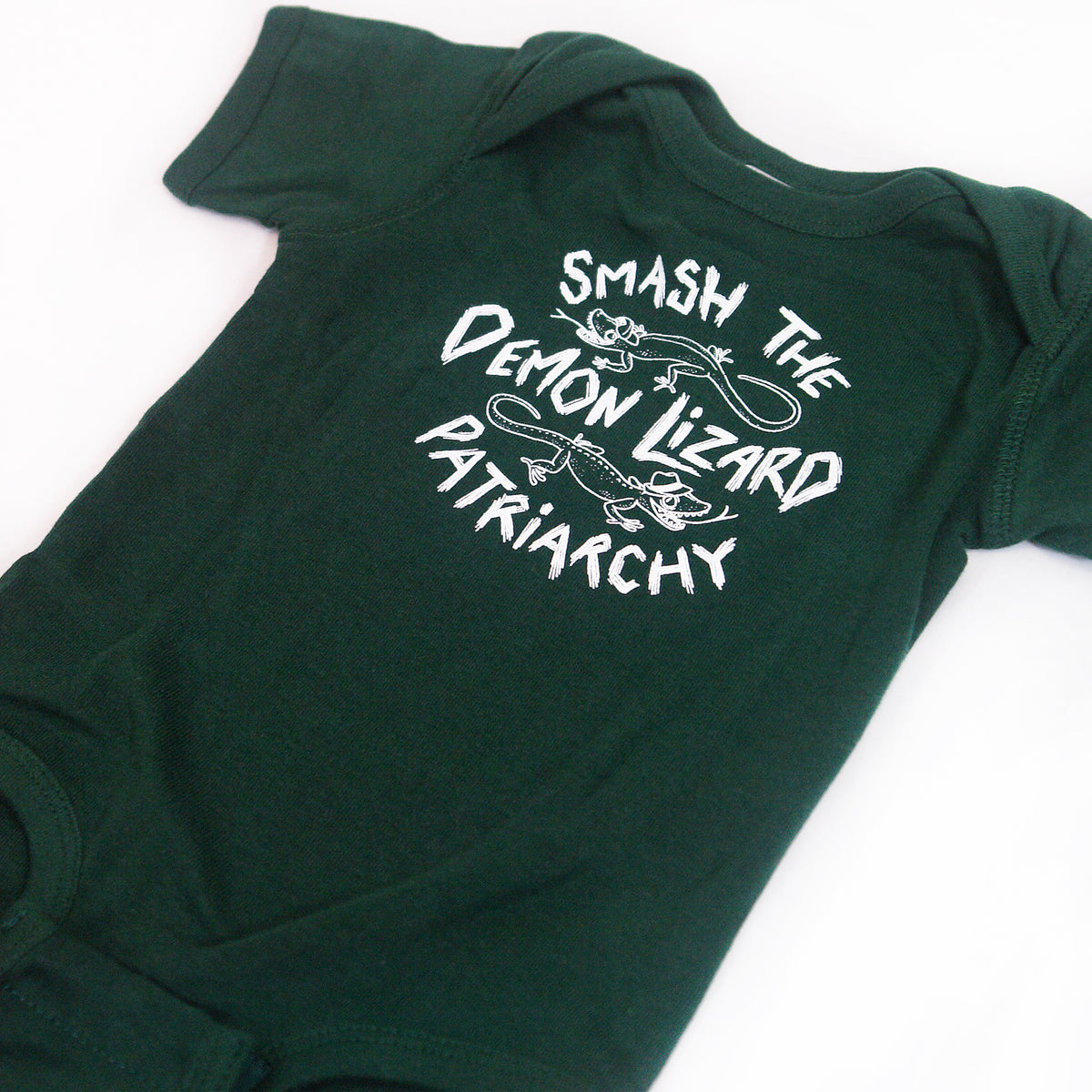 close up angled image of an emerald green tri blend baby onesie on a white background. onesie has center chest print in white that says smash the demon lizard patriarchy with two lizards