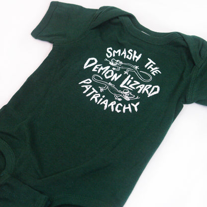 close up angled image of an emerald green tri blend baby onesie on a white background. onesie has center chest print in white that says smash the demon lizard patriarchy with two lizards
